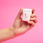 sosteniendo-el-gel-de-Bio-Oil-para-piel-seca-de-50ml.-Bote-blanco-con-etiqueta-visible-sobre-fondo-rosa.