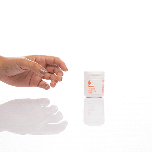 Bote-del-gel-Bio-Oil-de-50ml-en-una-superficie-reflectante.-A-la-izquierda-una-mano-con-brillo-en-la-palma.-Fondo-blanco.