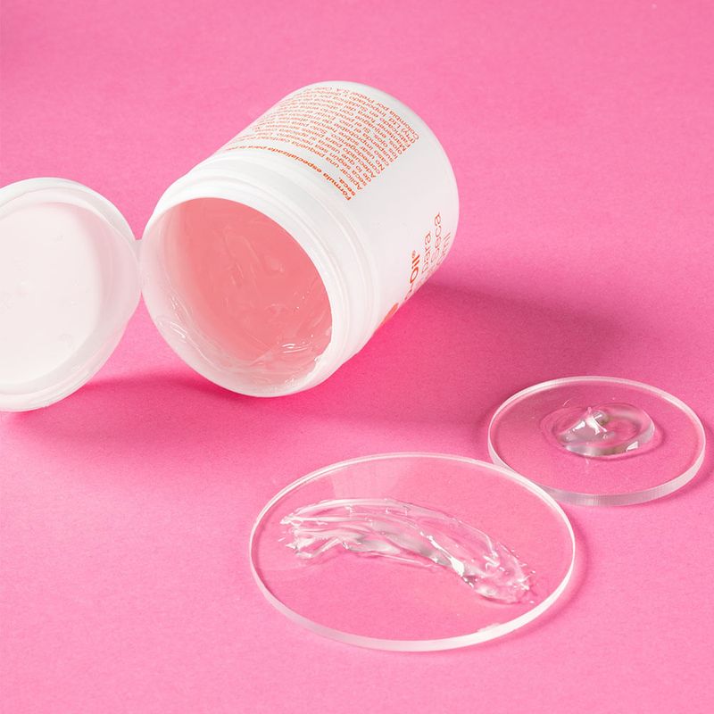 Gel-de-Bio-Oil-para-piel-seca-de-100ml-derramado-y-esparcido-sobre-dos-discos-transparentes.-El-bote-esta-abierto-e-inclinado-en-el-fondo-sobre-una-superficie-de-color-rosa-vibrante.