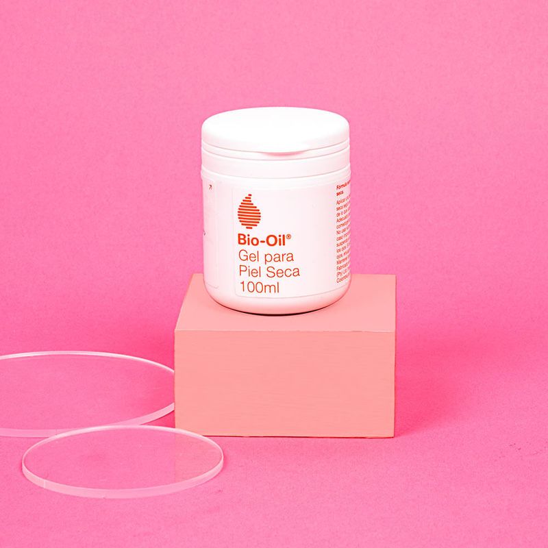 Bote-de-100ml-del-gel-para-piel-seca-Bio-Oil-colocado-sobre-un-bloque-rosa.-Alrededor-dos-discos-transparentes.-El-fondo-es-de-color-rosa-uniforme.